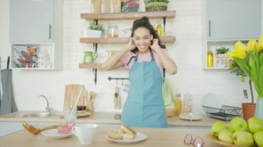 Genç bir kadın mutfakta aylaklık edip dans ediyor.