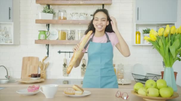 Mladá žena se poflakuje a zpívá s chlebem místo mikrofonu v kuchyni — Stock video