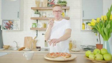 İtalyan gıda teslimatı için ticari. Genç adam etrafta dolaşıp mutfakta pizza yiyor.