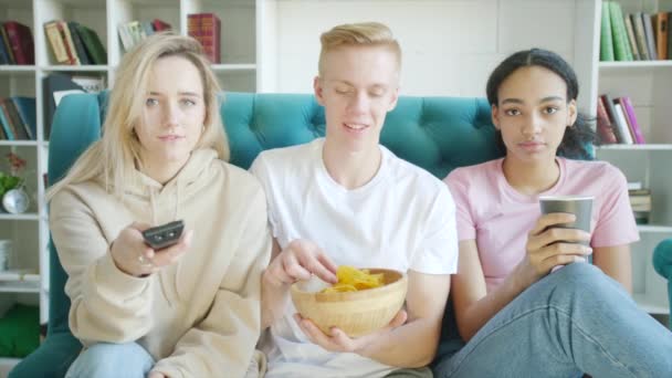Mutlu üç arkadaş tv izliyor ve kanepede birlikte aperatifler yiyor — Stok video