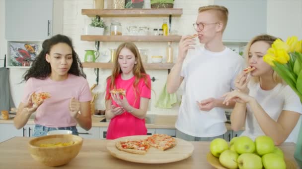 Gelukkige vrienden eten pizza en lachen in de keuken — Stockvideo