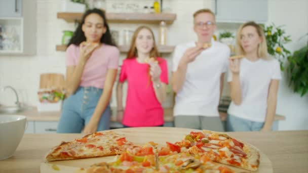 Italiaanse pizza op de voorgrond en groep tieners op de achtergrond in de keuken — Stockvideo