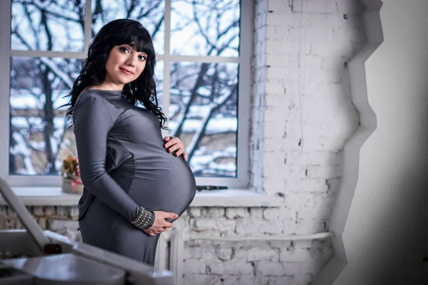 Těhotná Žena Stojí Okně Šedé Šaty Zimní Krajina Mimo — Stock fotografie