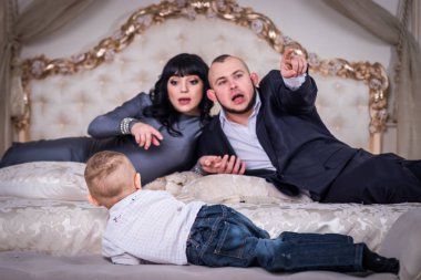 Bir iki yaşında oğlum yatağın kenarında oturur. Baba ve hamile anne onu arkadan izliyor. Çocuk üzücü.