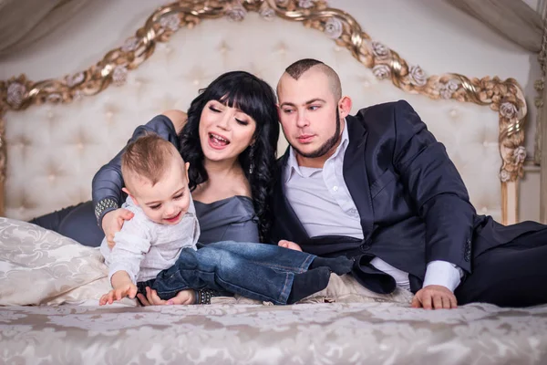 Happy family in the bedroom. The father tickles his two-year-old son, the pregnant mother looks at them with a happy look...