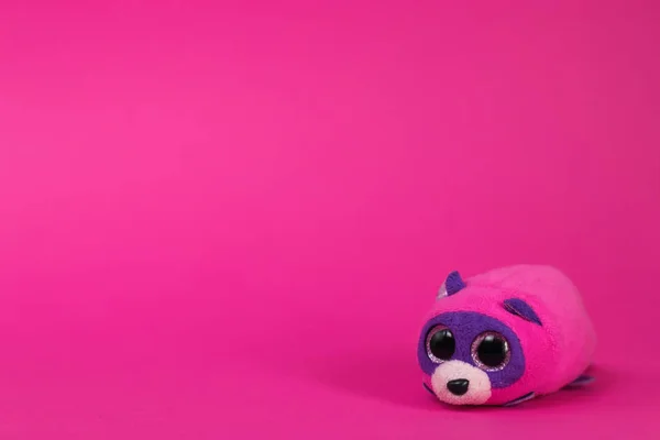 Toy cartoon pink and purple mouse sits on a pink background.