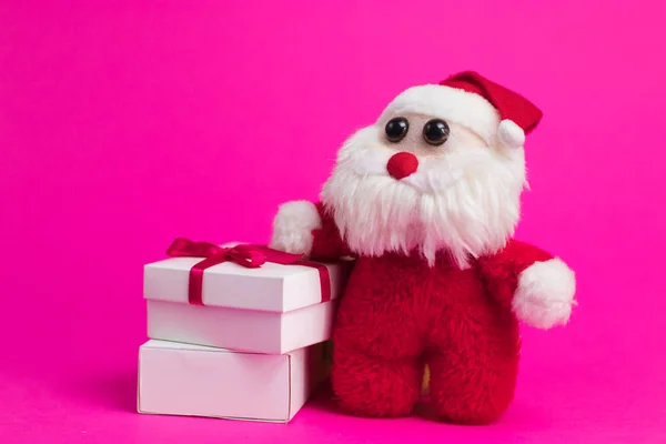 Toy cartoon santa with white gift boxes on a pink background.