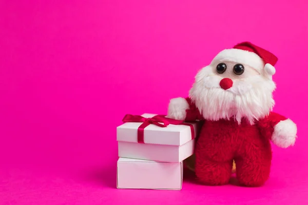 Toy cartoon santa with white gift boxes on a pink background.