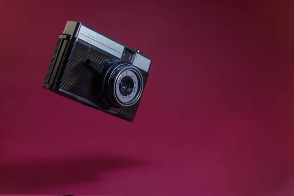 Old retro camera on red background flying in air.