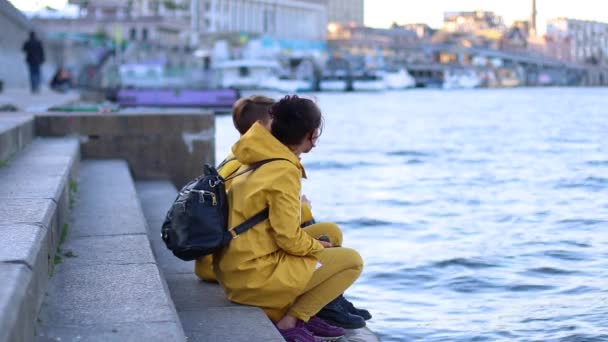 Två unga flickor i gula jackor sitter på piren — Stockvideo