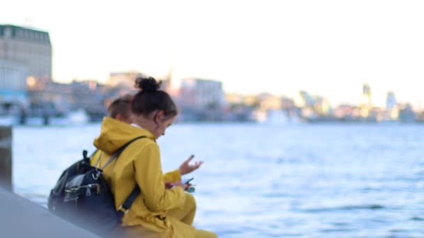 两个穿着黄色夹克的小女孩坐在码头上 — 图库视频影像