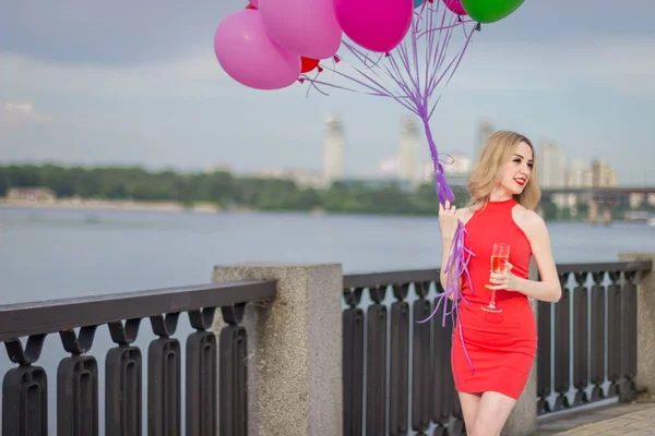 Une fille se tient près de la rivière avec des ballons et un réservoir de champagne — Photo