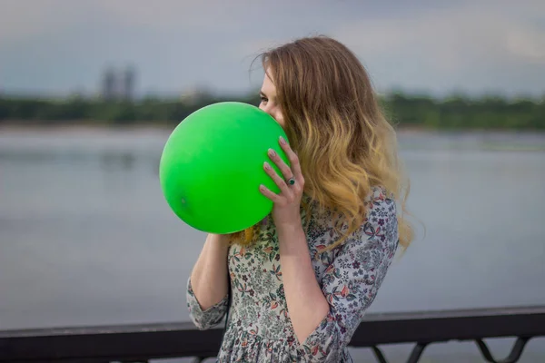 Chica infla una pelota contra el fondo de un río — Foto de Stock