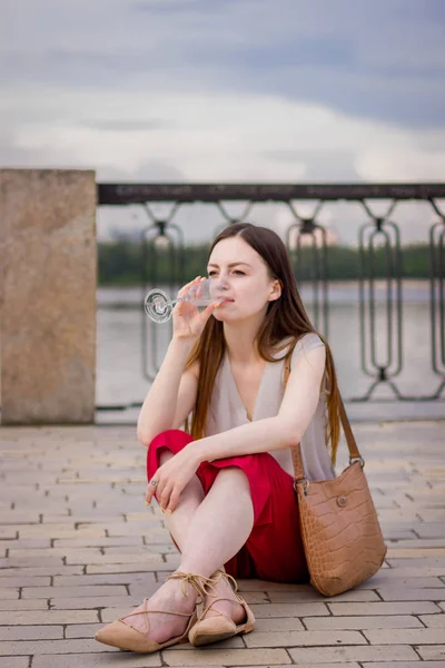 Дівчина сидить біля річки з келихом шампанського — стокове фото