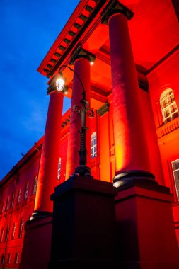 Gece sokağında, penceresi olan bir evin duvarındaki direkte parlayan kırmızı fener.