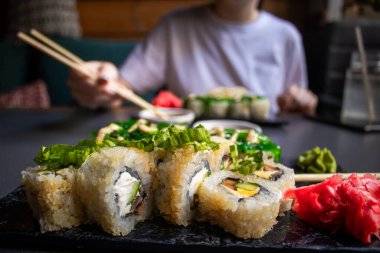 Yakından bakınca bambu çubuklarını soya sosuyla ıslatırken nigiri karidesli tutuyor. Lokantada ahşap tepside suşi hazırlarken Nigiri 'yi soya sosuna batırmak. Japon mutfağı kavramı.