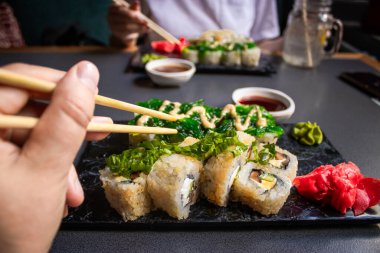 Yakından bakınca bambu çubuklarını soya sosuyla ıslatırken nigiri karidesli tutuyor. Lokantada ahşap tepside suşi hazırlarken Nigiri 'yi soya sosuna batırmak. Japon mutfağı kavramı.