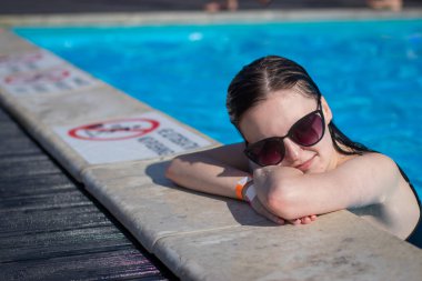 Güneş gözlüklü genç bir kız havuzda yüzüyor. Güzel bir kadın açık havuzda suda dinleniyor.