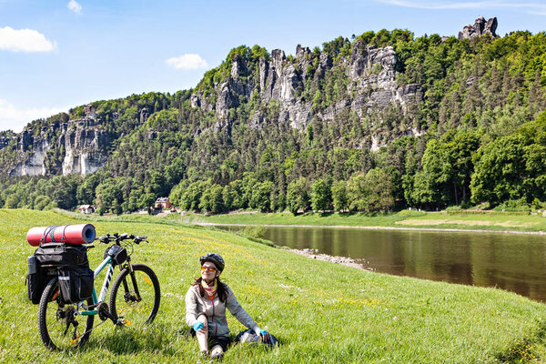 Woman cyclist with loaded bicycle having break while travelling.