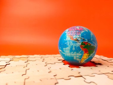 The image shows a colorful globe, which is a puzzle, resting on a surface covered with scattered, unassembled puzzle pieces.