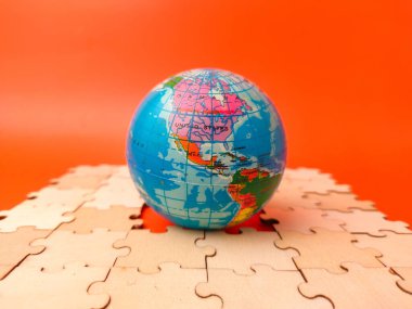 Closeup colorful globe, which is a puzzle, resting on a surface covered with scattered, unassembled puzzle pieces.
