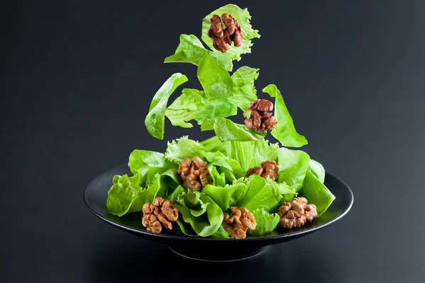 Yeşil salata parçalar ve ceviz plaka, yaratıcı karanlık bir arka plan üzerinde atış yukarıda havaya kaldırmak. Yeşil salata ile ceviz. Stok Fotoğraf