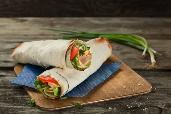 Tortilla wrap or wrap sandwich with ham and vegetables close up. Roll sandwich with meat and green salad