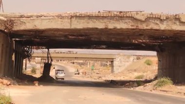 Halep, Suriye 'deki yıkılmış ve çürümüş köprü, çelik parmaklıklar ve ağır savaş hasarı ile. Sivillerin savaşa, direnişe, cesarete ve hayatta kalmaya nasıl uyum sağladığını yansıtan normal bir arabanın altından bir araba geçiyor..