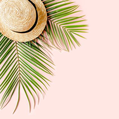 Yaz dönemi. Tropik palmiye yaprağı dalları, pembe arka planda hasır şapka ve mesaj için boş alan. Seyahat tatili konsepti. Düz yatış, üst görünüm.