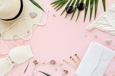 Kadınsı beyaz mayo plaj aksesuarları, pembe arka planda tropikal palmiye yaprağı dalları. Seyahat tatili konsepti. Yaz dönemi. Yol çerçevesi ayarlandı