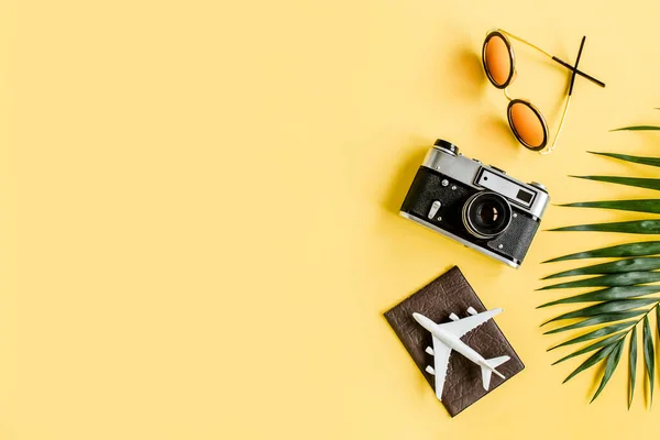 Traveler accessori concetto su sfondo giallo. Fotocamera retrò, modello di aereo, aereo e foglia di palma tropicale. — Foto Stock