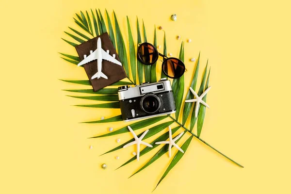 黄色背景下的旅行配件概念。采购产品复古相机，模型飞机，太阳镜，护照和热带棕榈叶。夏季背景. — 图库照片
