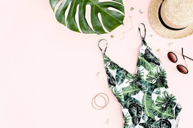 Kadın plaj aksesuarları: tropik baskılı mayo, pembe arka planda hasır şapka. Yaz dönemi. Düz yatıyordu