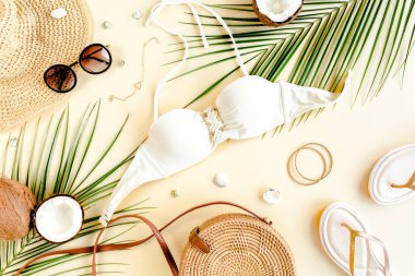 Kadın plaj aksesuarları: bikini, rattan çanta, hasır şapka, sarı arka planda tropik palmiye yaprakları. Yaz arkaplanı. 