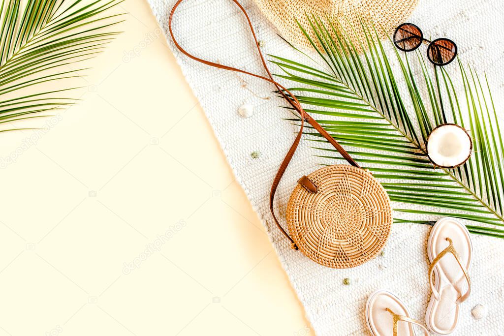 Womans beach accessories: rattan bag, straw hat, tropical palm leaves on yellow background. Summer background. 