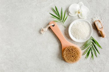 Spa konsepti. Doğal organik spa ürünleri, deniz tuzu, masaj fırçası ve yukarıdaki gri mermer masada tropik palmiye yaprakları. Spa arkaplanı