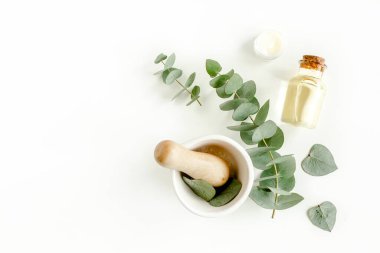 Bir şişe okaliptüs esaslı yağ, beyaz arka planda okaliptüs yaprakları. Doğal organik kozmetik ürünleri. Düz yatış, üst görünüm.