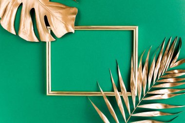 Altın tropikal palmiye yeşil arka planda Monstera ve fotoğraf çerçevesi bırakır. Düz konum, üst görünüm minimum konsept.