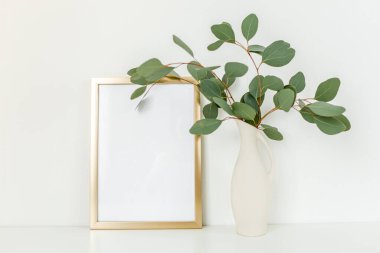 Boş çerçeve modeli ve okaliptüs dalları açık arkaplanda, vazoda. Ev dekoru. Günlük, web sitesi veya sosyal medya kavramı.