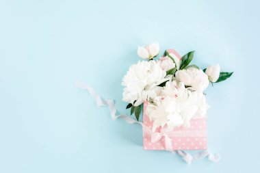 Mavi arka planda çiçekler için bir zarf içinde beyaz şakayık demeti. Minimum çiçek konsepti tebrik kartı. Düz yatış, üst görünüm. 