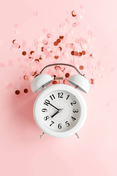 ピンクの背景に金色のコンフェッティを覆った白い目覚まし時計をトップビュー。テンプレート｜フェミニンなブログソーシャルメディア。ミニマルなスタイル。平置き — ストック写真