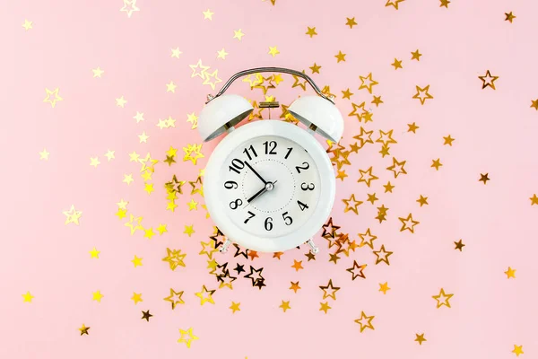 Alarm clock covered golden stars confetti, decoration on a pink, festive background. Christmas or New Year pattern. Colorful celebration, birthday. — Stock Photo, Image
