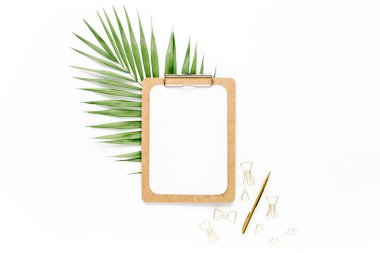 Beyaz arka planda tropikal yaprakları, panosu ve aksesuarları olan ev ofisinin çalışma alanı modeli. Düz yatış, üst görünüm