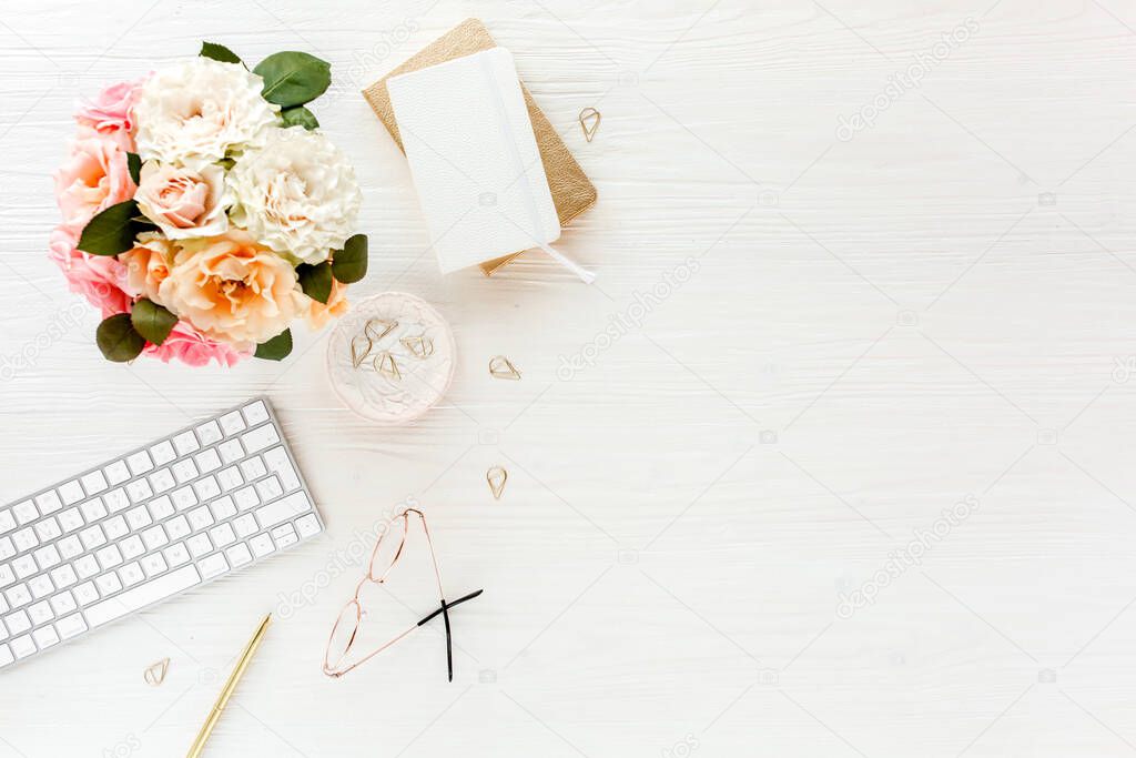 Womens workspace with pink and beige roses flowers bouquet, accessories, diary, glasses on white background. Flat lay, top view. Beauty blog concept.