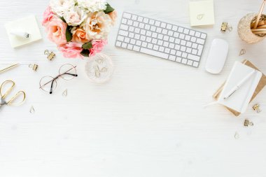Düz uzanmış kadınların ofis masası. Bilgisayarlı kadın çalışma alanı, pembe güller çiçekler, aksesuarlar, altın günlük, beyaz arka planda gözlük. Üst görünüm 