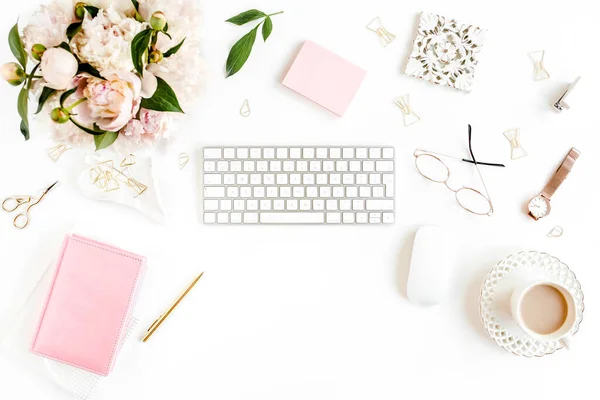 Flach lag der Schreibtisch. Weiblicher Arbeitsplatz mit Computer, rosa Pfingstrosenstrauß, Accessoires auf weißem Hintergrund. Weiblicher Hintergrund von oben. — Stockfoto