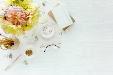 Düz uzanmış kadınların ofis masası. Bilgisayarlı kadın çalışma alanı, pembe ve sarı güller çiçekler, aksesuarlar, günlük, beyaz arka planda gözlük. Üst görünüm