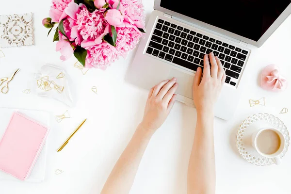 Espacio de trabajo femenino con manos femeninas, portátil, ramo de peonías rosadas, accesorios sobre fondo blanco. Vista superior de fondo femenino. Puesta plana. —  Fotos de Stock