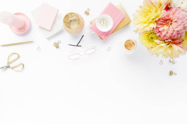 Ev ofisinin masası düzdü. Pembe ve bej gülleri, çiçekleri, aksesuarları, altın ve pembe günlüğü, beyaz ahşap arka planı olan kadın çalışma alanı. Üst görünüm 