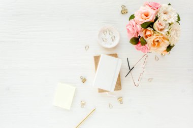 Düz uzanmış kadınların ofis masası. Pembe güller, çiçek buketi, aksesuarlar, altın günlük, beyaz ahşap arka planda gözlük.